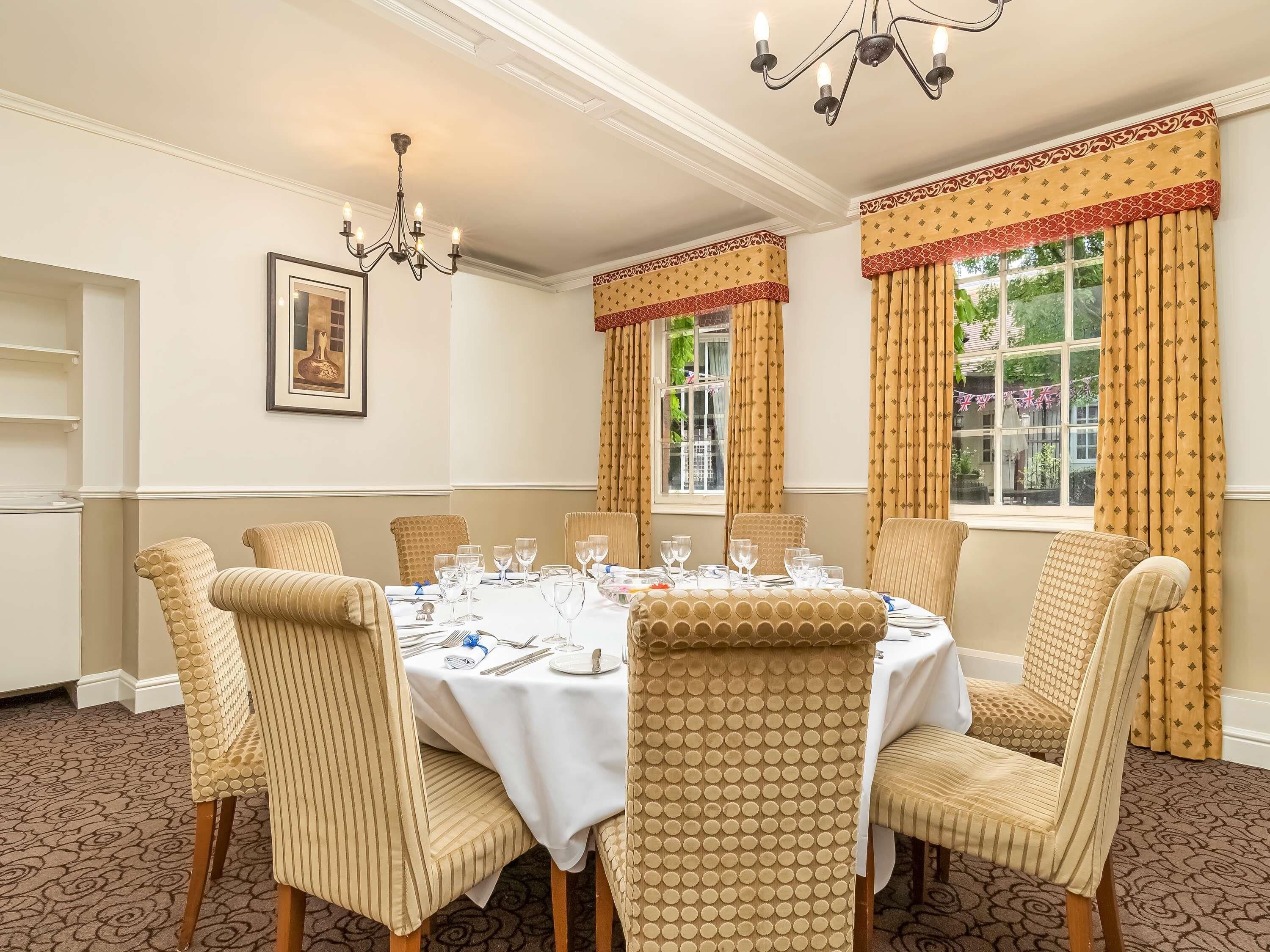 A dining room with a round table set for six, surrounded by six chairs, a chandelier, and a framed picture on the wall.