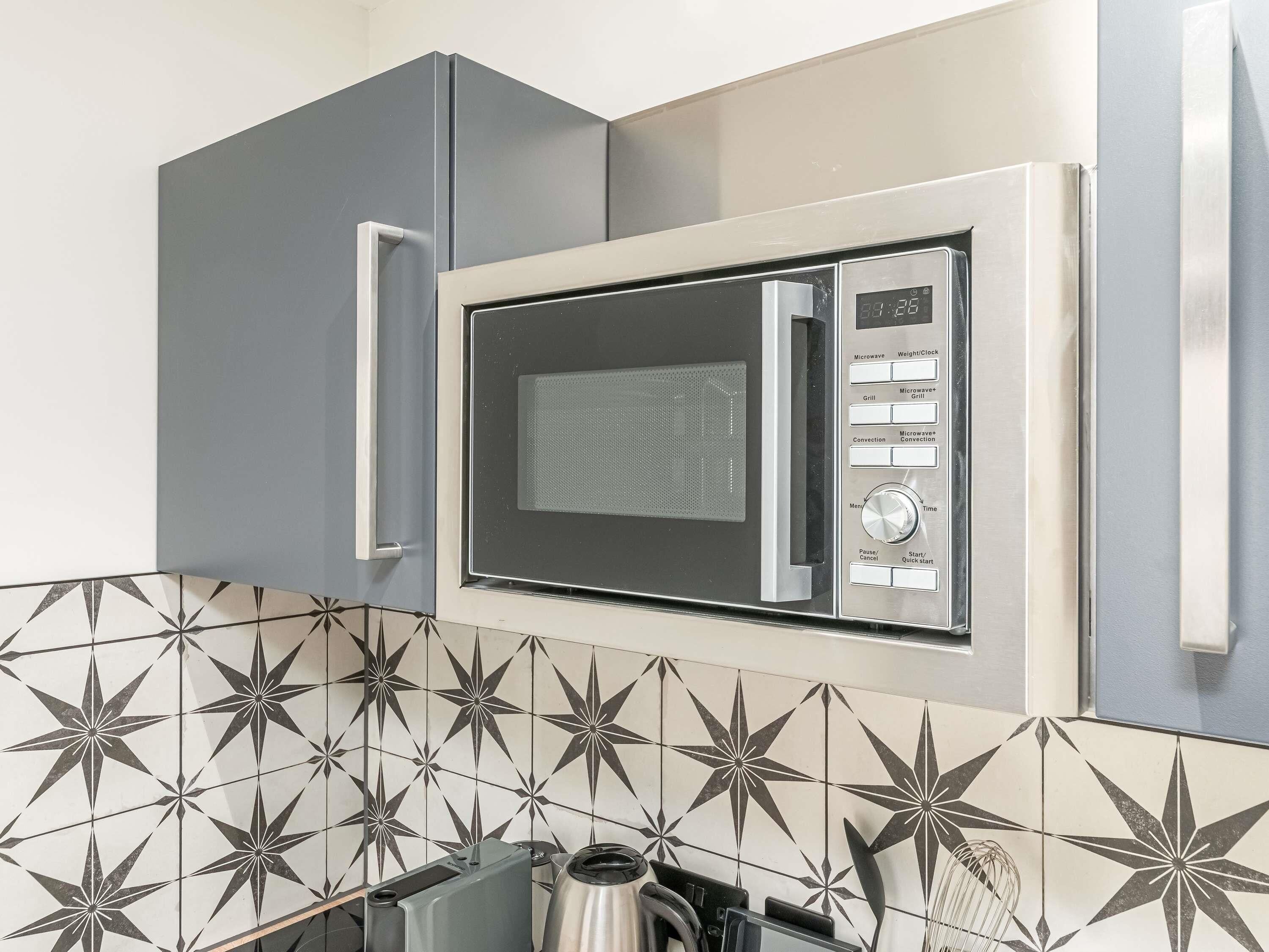 A kitchen with a built-in microwave, a kettle, and a toaster.