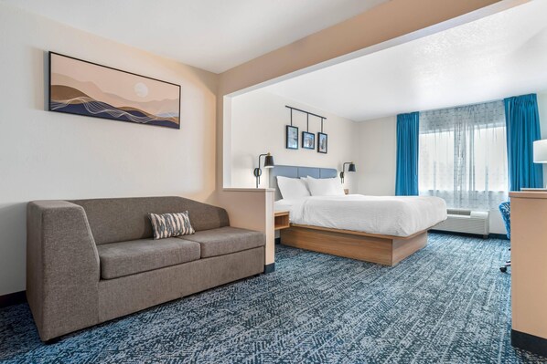 Habitación de hotel con sofá, cama, escritorio y ventana con cortinas.