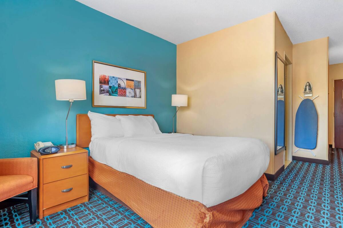 A hotel room with a bed, bedside tables, a chair, a framed picture on the wall, and a patterned floor.