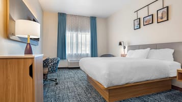 Habitación de hotel con cama, escritorio, silla, lámpara, ventana con cortinas e imágenes enmarcadas en la pared.