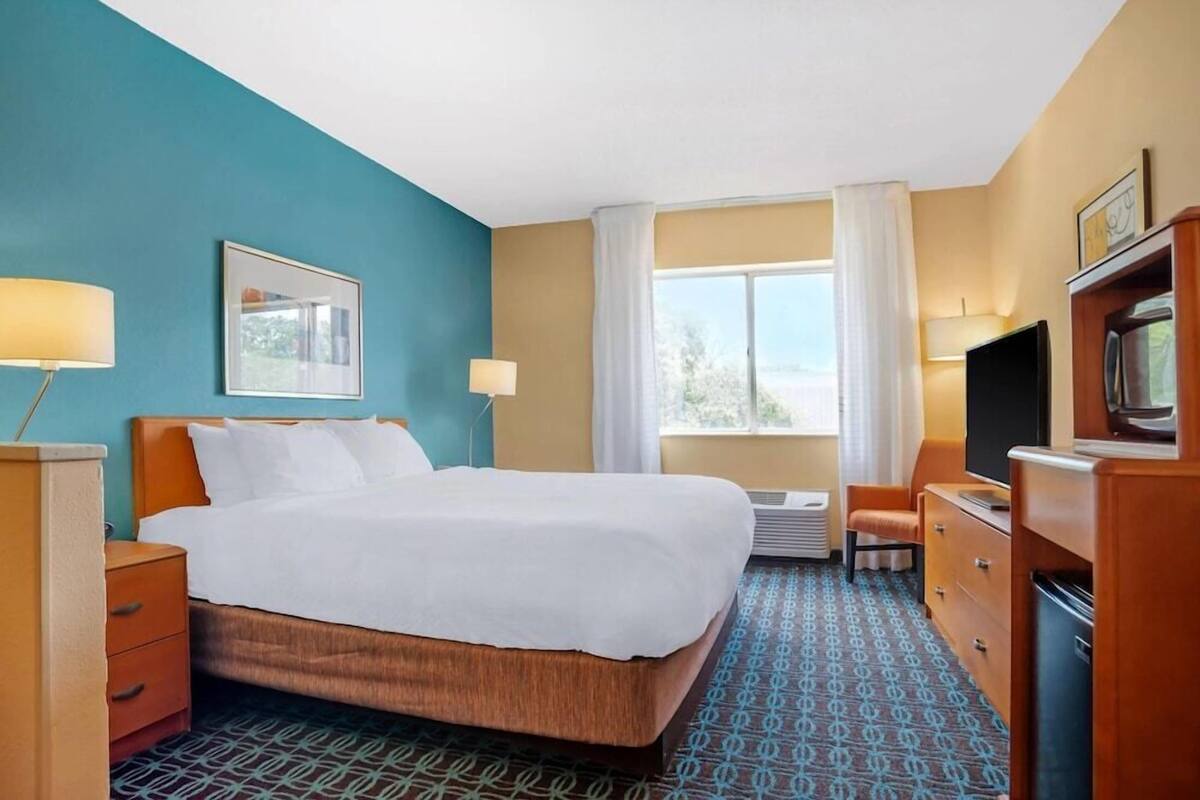 A hotel room with a bed, a desk, a television, and a window with curtains.
