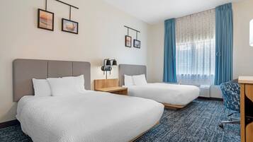 Habitación de hotel con dos camas, un escritorio, una silla y una ventana con cortinas.