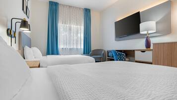 A hotel room with two beds, a desk, a chair, a TV, and a window with curtains.