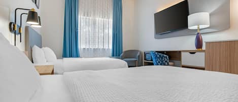 A hotel room with two beds, a desk, a chair, a TV, and a window with curtains.
