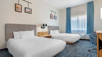 A hotel room with two beds, a desk, a chair, a window with curtains, and wall-mounted artwork.