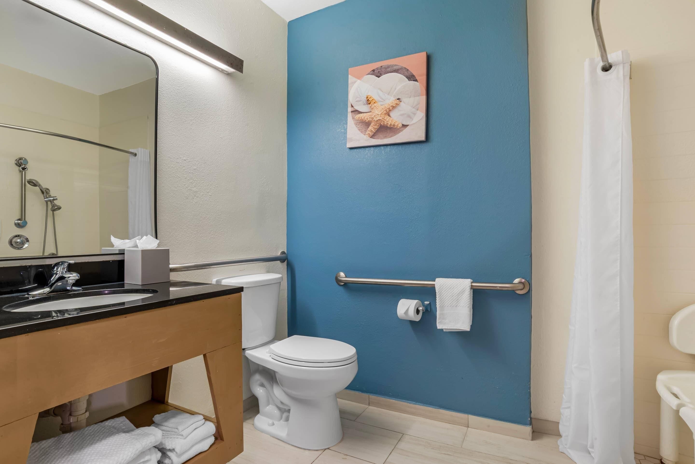 Casa de banho com sanita, lavatório e chuveiro. Tem um suporte para toalhas e um porta-papel higiénico.