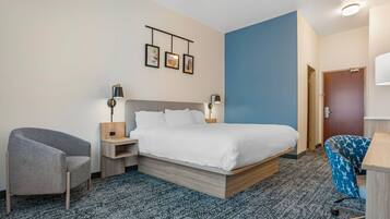 Una habitación de hotel con cama, una silla, un escritorio, una lámpara y un cuadro colgado en la pared.