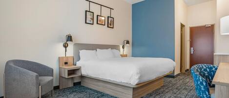 Une chambre d’hôtel avec un lit, une chaise, un bureau, une lampe et un tableau accroché au mur.