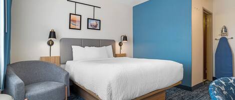 A hotel room with a bed, two bedside lamps, a chair, a blue accent wall, and a door.