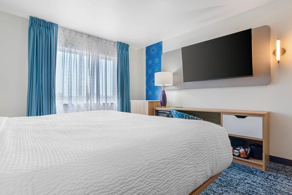 A hotel room with a large bed, a flat-screen TV mounted on the wall, a bedside table with a lamp, and a built-in wardrobe.