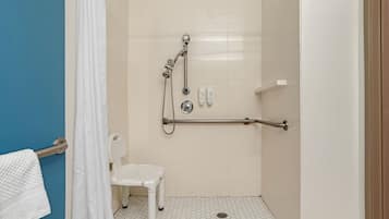 A shower with a grab bar, a white chair, and a toilet.