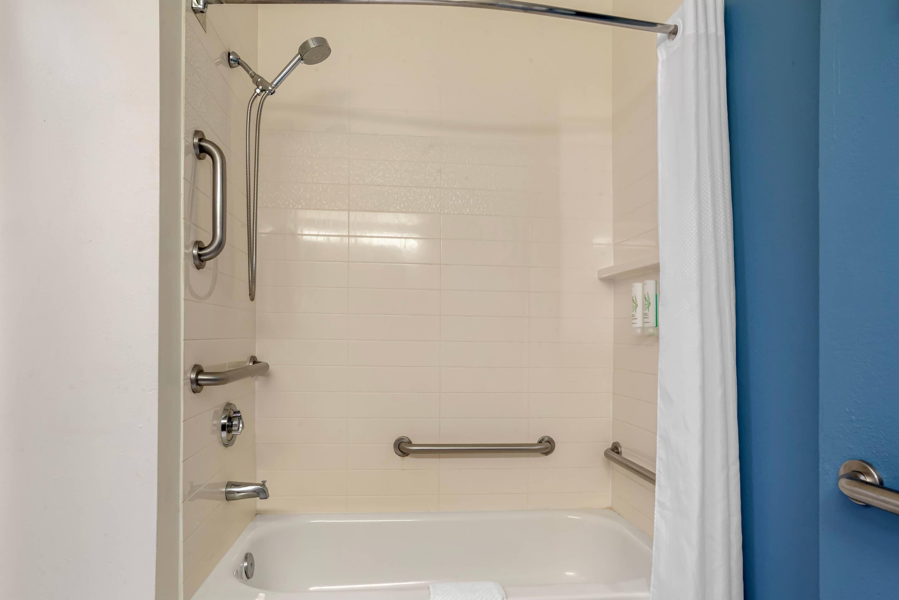 Baño con ducha, barras de apoyo y bañera.