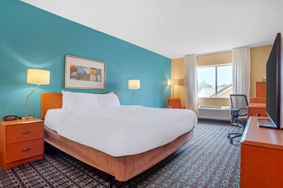 A hotel room with a bed, two bedside tables with lamps, a desk with a chair, a television, and a window with curtains.