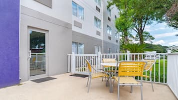 A balcony with a table and chairs, a white railing, and a building with multiple windows and vents.