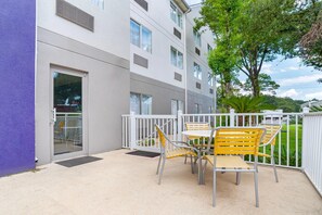 A balcony with a table and chairs, a white railing, and a building with multiple windows and vents. - Sleep Inn & Suites Pensacola - University Area (Pensacola)