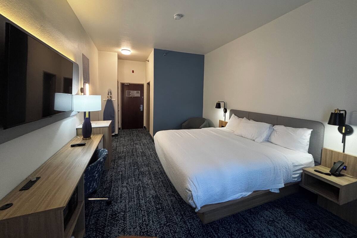 A hotel room with a bed, bedside tables, a desk, a chair, a mirror, and a door.