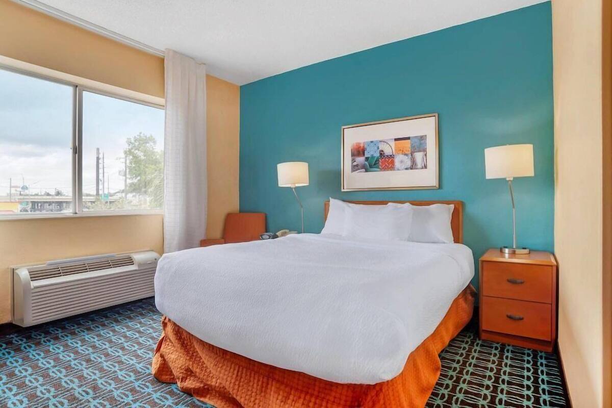 A hotel room with a bed, two bedside tables, a window, and a wall-mounted picture.