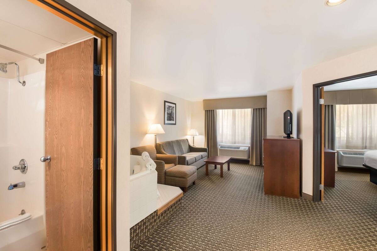 A hotel room with a wooden door, a bathtub, a sofa, a coffee table, and a TV.