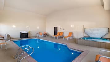 An indoor swimming pool with a clear blue water, surrounded by lounge chairs and a hot tub.