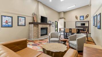 A hotel lobby with leather sofas, a fireplace, a dining area, and ski-themed wall art.