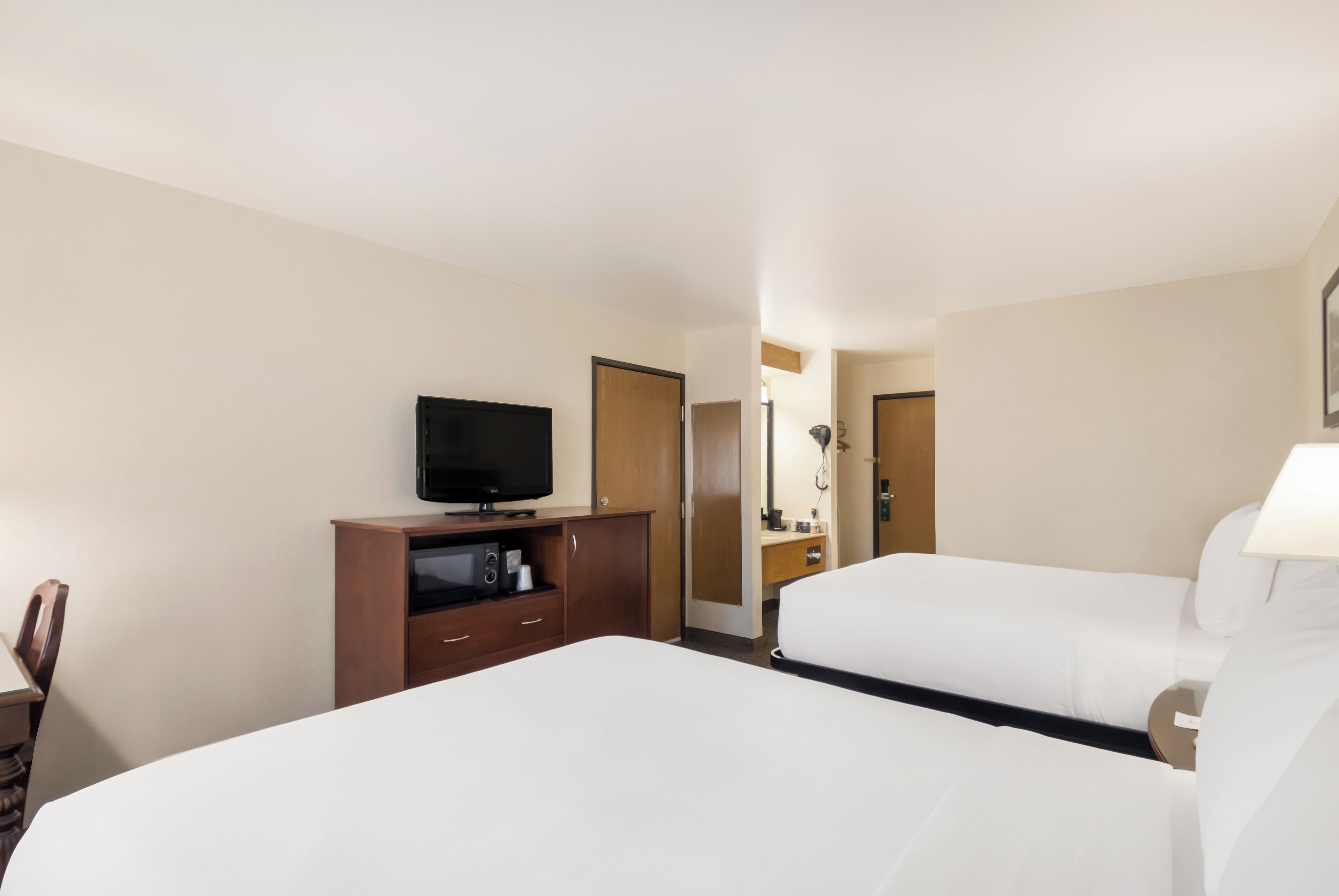A hotel room with two beds, a TV, a desk with a computer, and a bathroom visible through an open door.