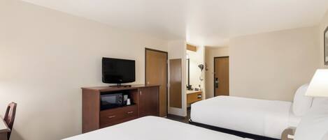 A hotel room with two beds, a TV, a desk with a computer, and a bathroom visible through an open door.
