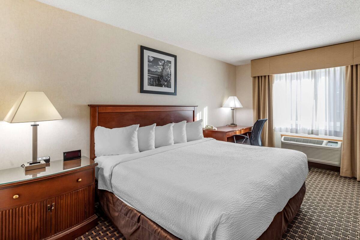 A hotel room with a large bed, bedside tables, a desk, and a window with curtains.