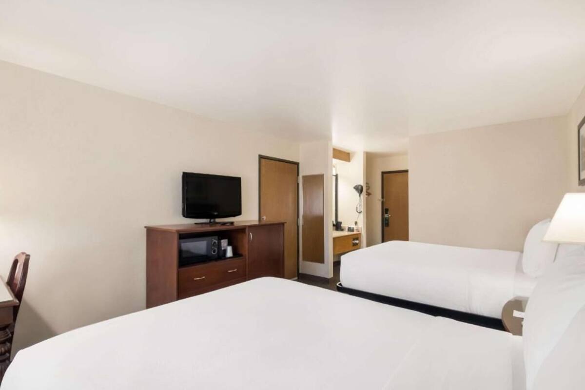 A hotel room with two beds, a TV, a desk, and a mirror.