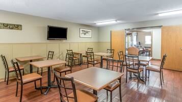 A dining area with multiple tables and chairs, a television mounted on the wall, and a framed picture.