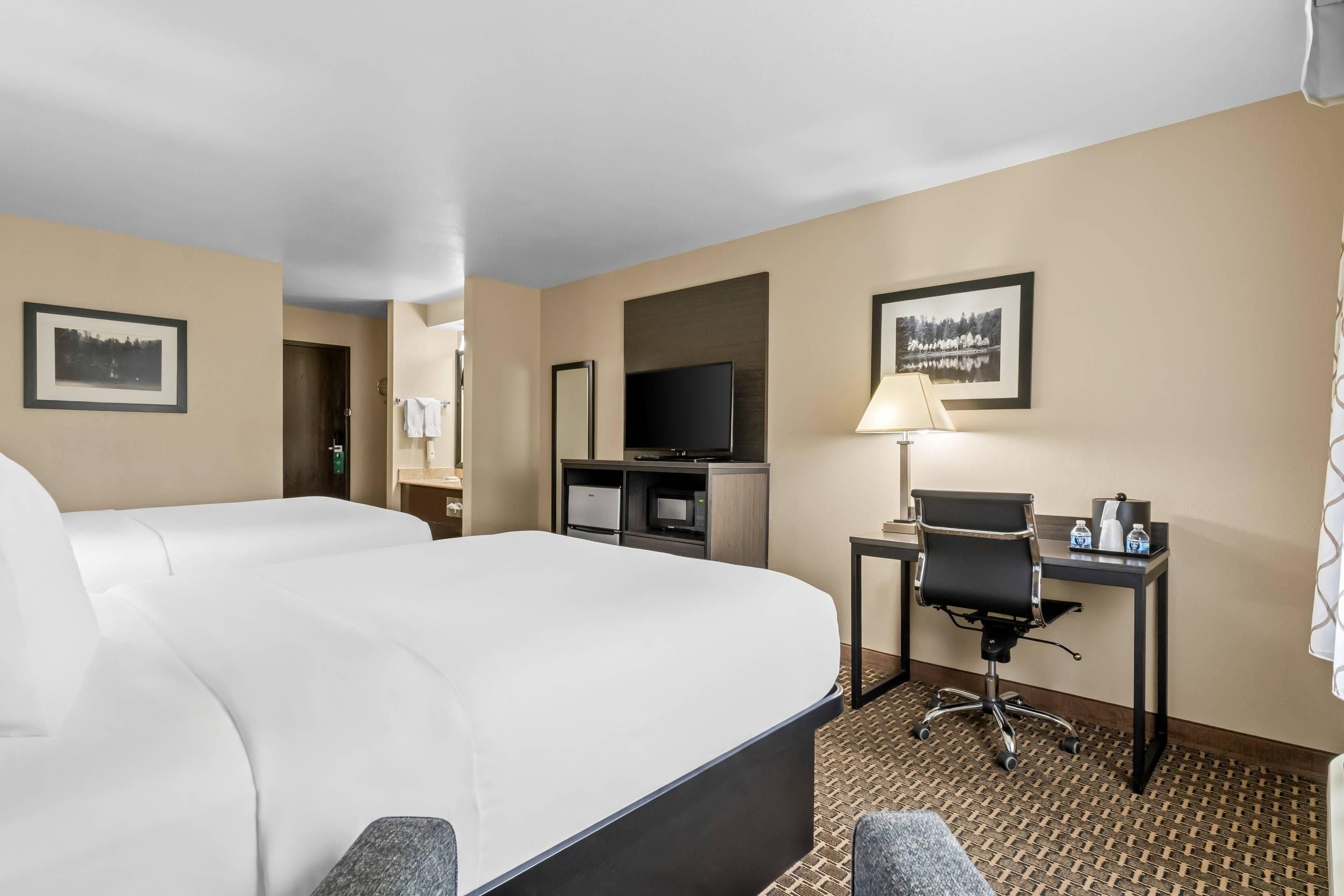 A hotel room with a large bed, a desk with a chair, a television, and framed pictures on the walls.