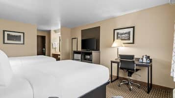 A hotel room with a large bed, a desk with a chair, a television, and framed pictures on the walls.