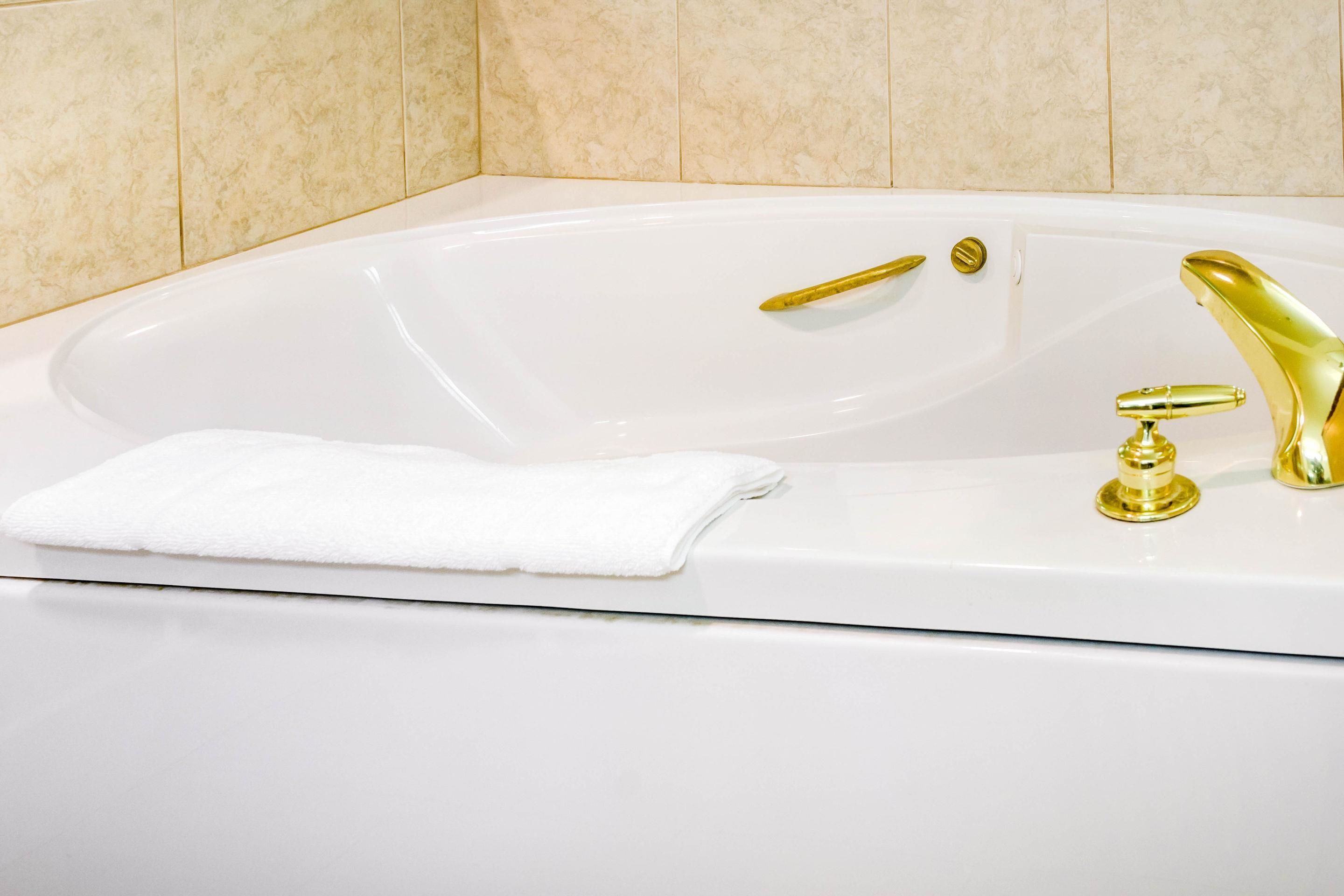 A white bathtub with gold fixtures and a white towel.