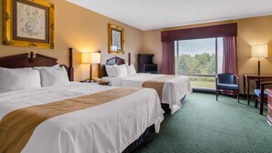 A hotel room with two beds, a desk, a chair, a lamp, and a large window with a view of trees. - Quality Inn & Suites Carthage near Precious Moments Chapel (Carthage)