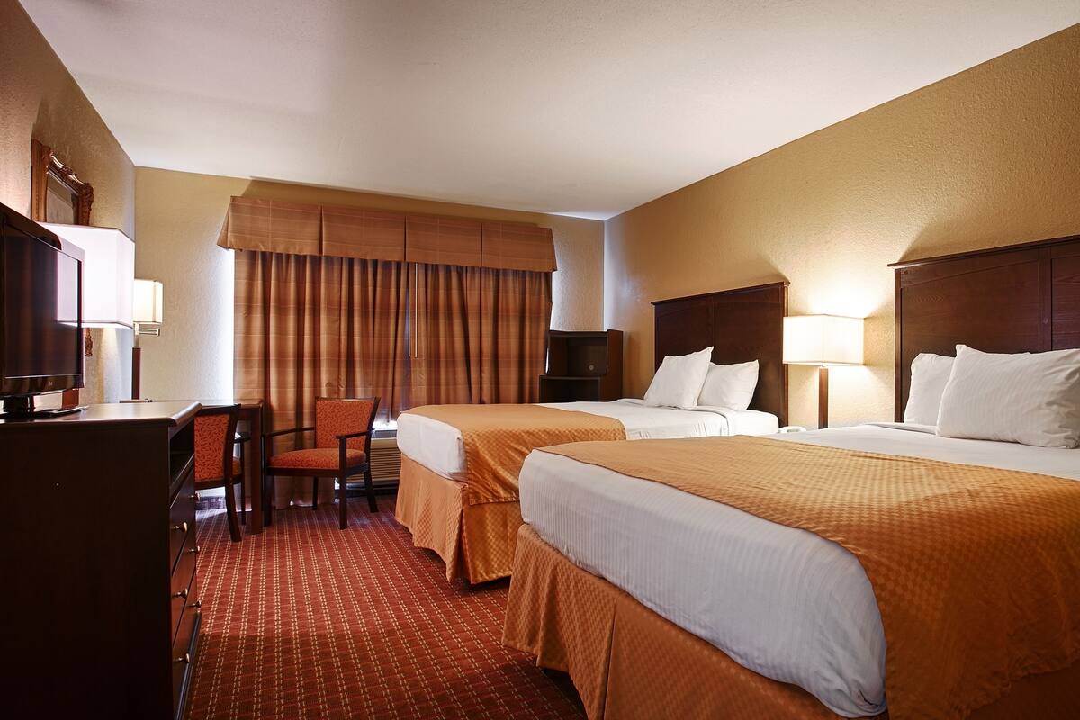 Una habitación de hotel con dos camas, un escritorio, una silla y un televisor.