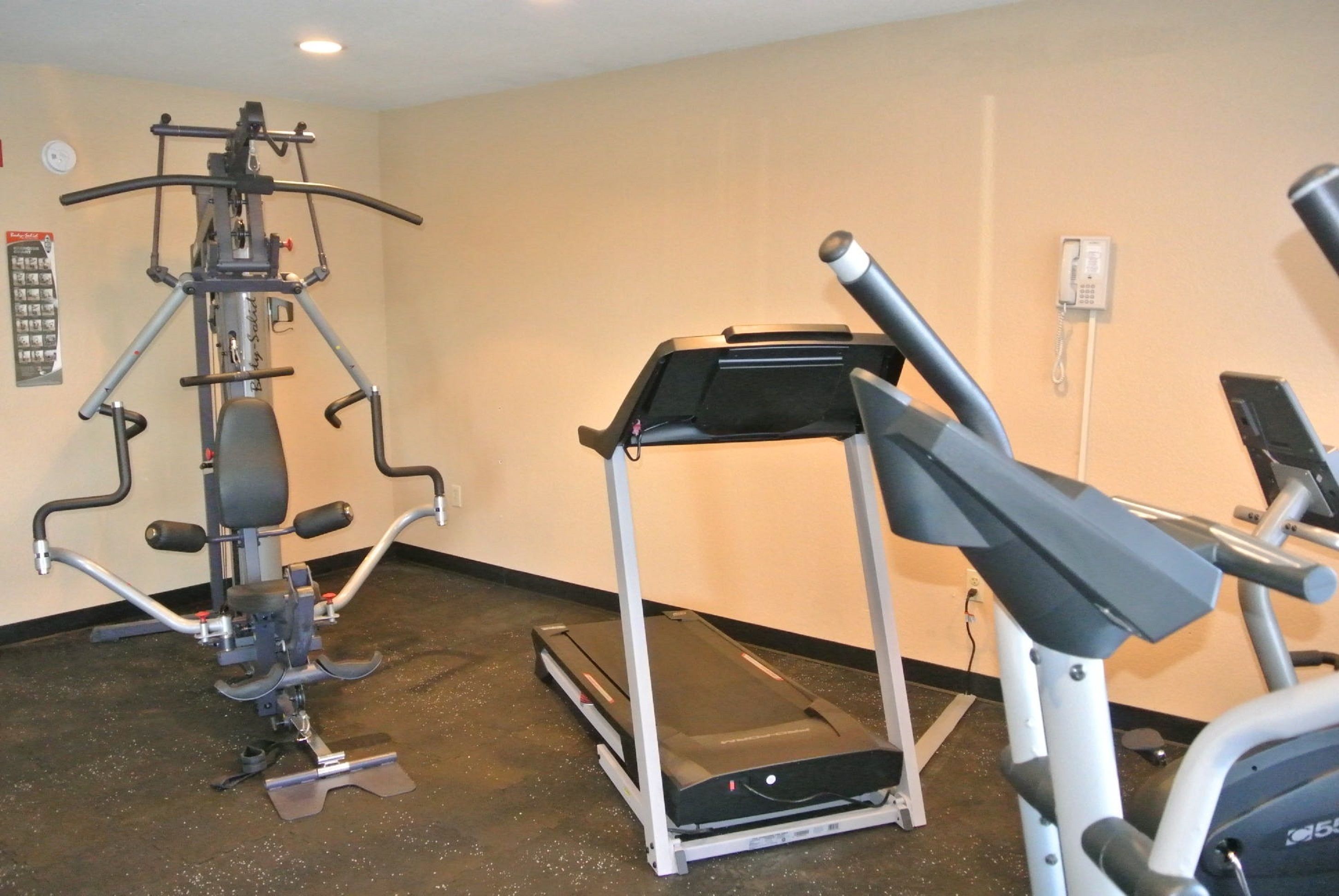A gym with a treadmill, a multi-functional exercise machine, and a wall-mounted phone.