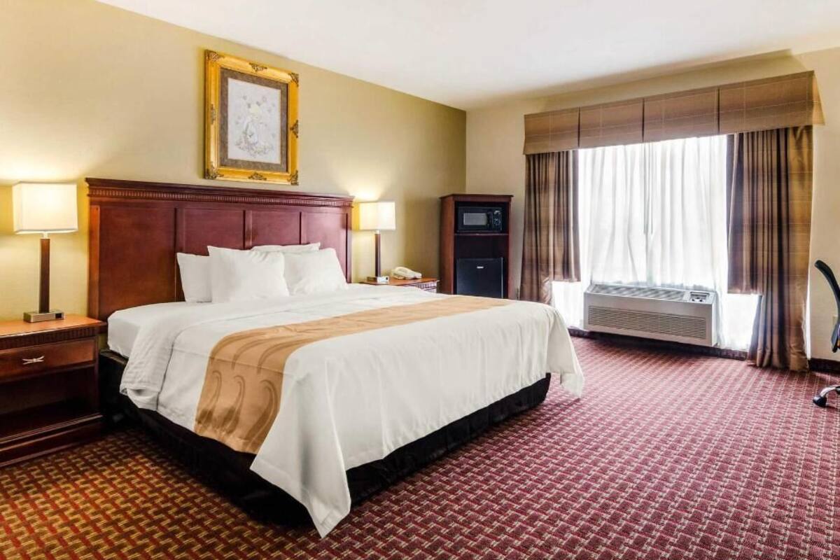 Habitación de hotel con una cama grande, lámparas de noche, televisión, equipo de aire acondicionado y una ventana con cortinas.