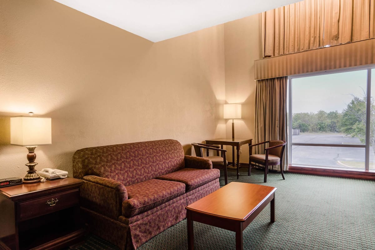 Habitación de hotel con sofá, una mesita, lámpara, teléfono y ventana con vistas al exterior.