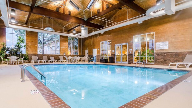 An indoor swimming pool with a brick border, lounge chairs, and a view of the outdoors through large windows. - Quality Inn & Suites Carthage near Precious Moments Chapel (Carthage)