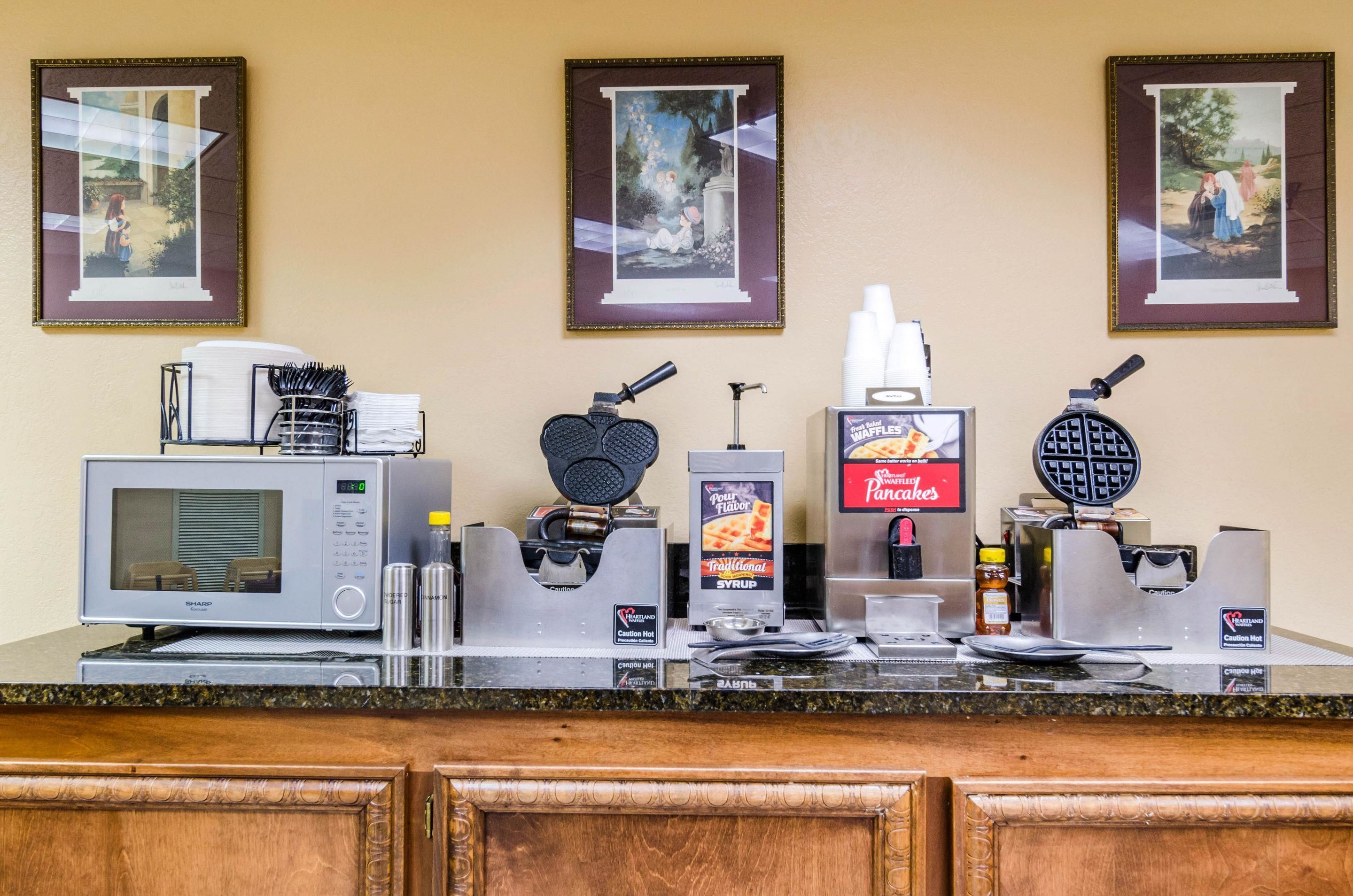 A breakfast bar with a microwave, waffle maker, and syrup dispenser.