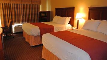 A hotel room with two beds, a desk, a chair, a lamp, and a television.