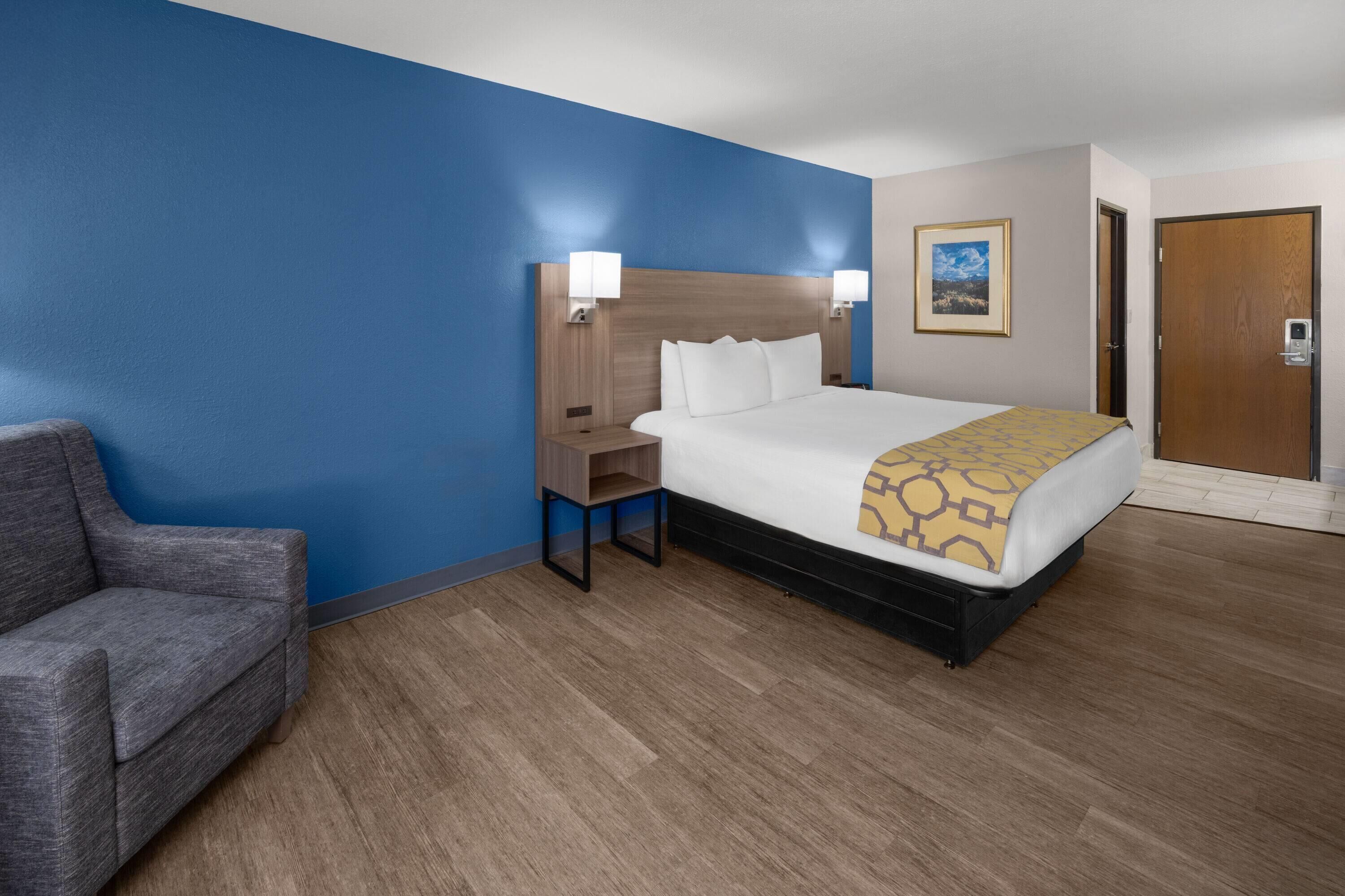 A hotel room with a bed, a nightstand, a chair, and a door.