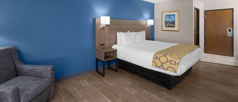 A hotel room with a bed, a nightstand, a chair, and a door.