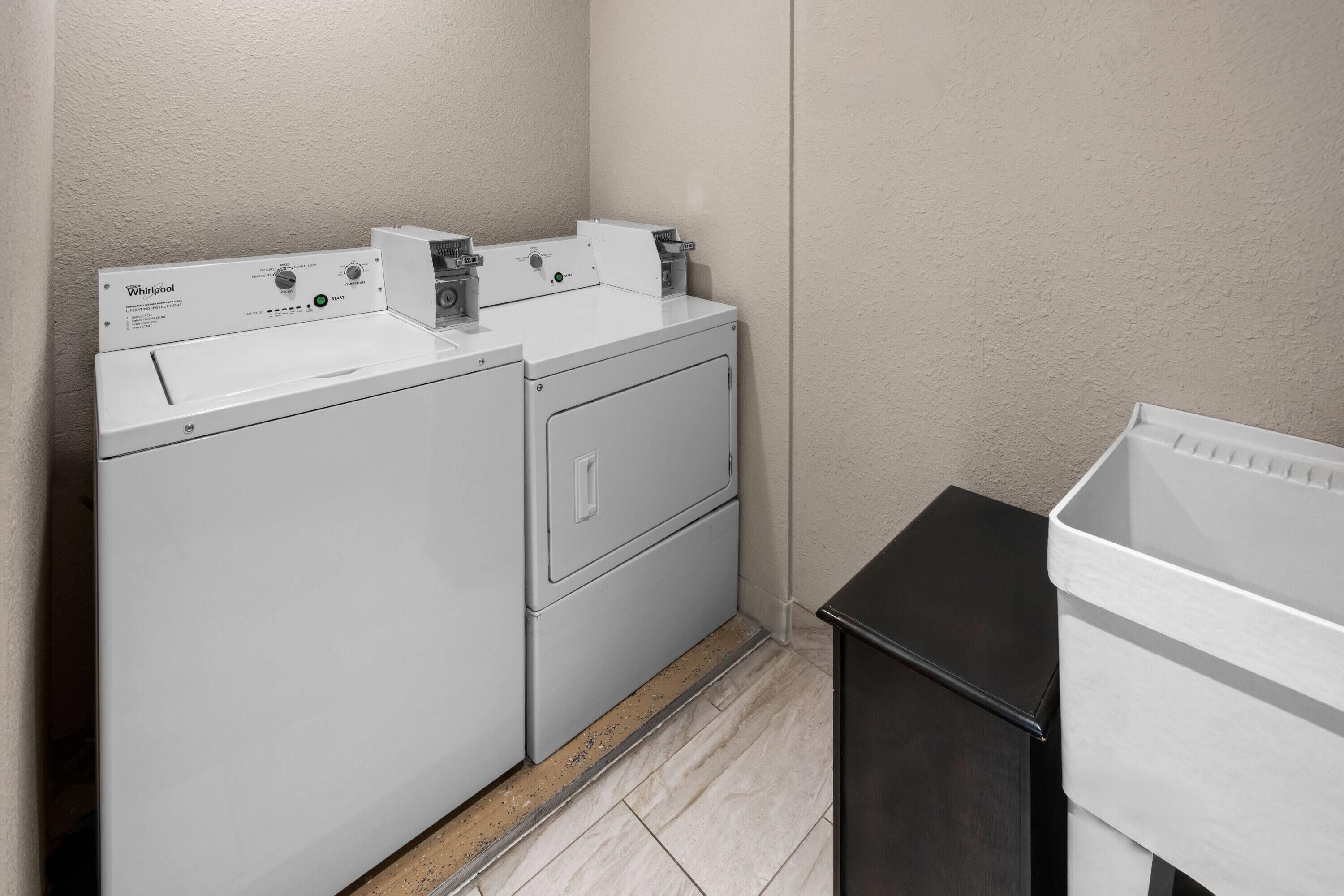 Un espace buanderie équipé d’un lave-linge et d’un sèche-linge Whirlpool, d’une poubelle noire et d’un bac de rangement blanc.