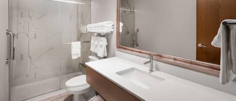 Un baño moderno con cabina de ducha de vidrio, un lavamanos blanco y un espejo grande.