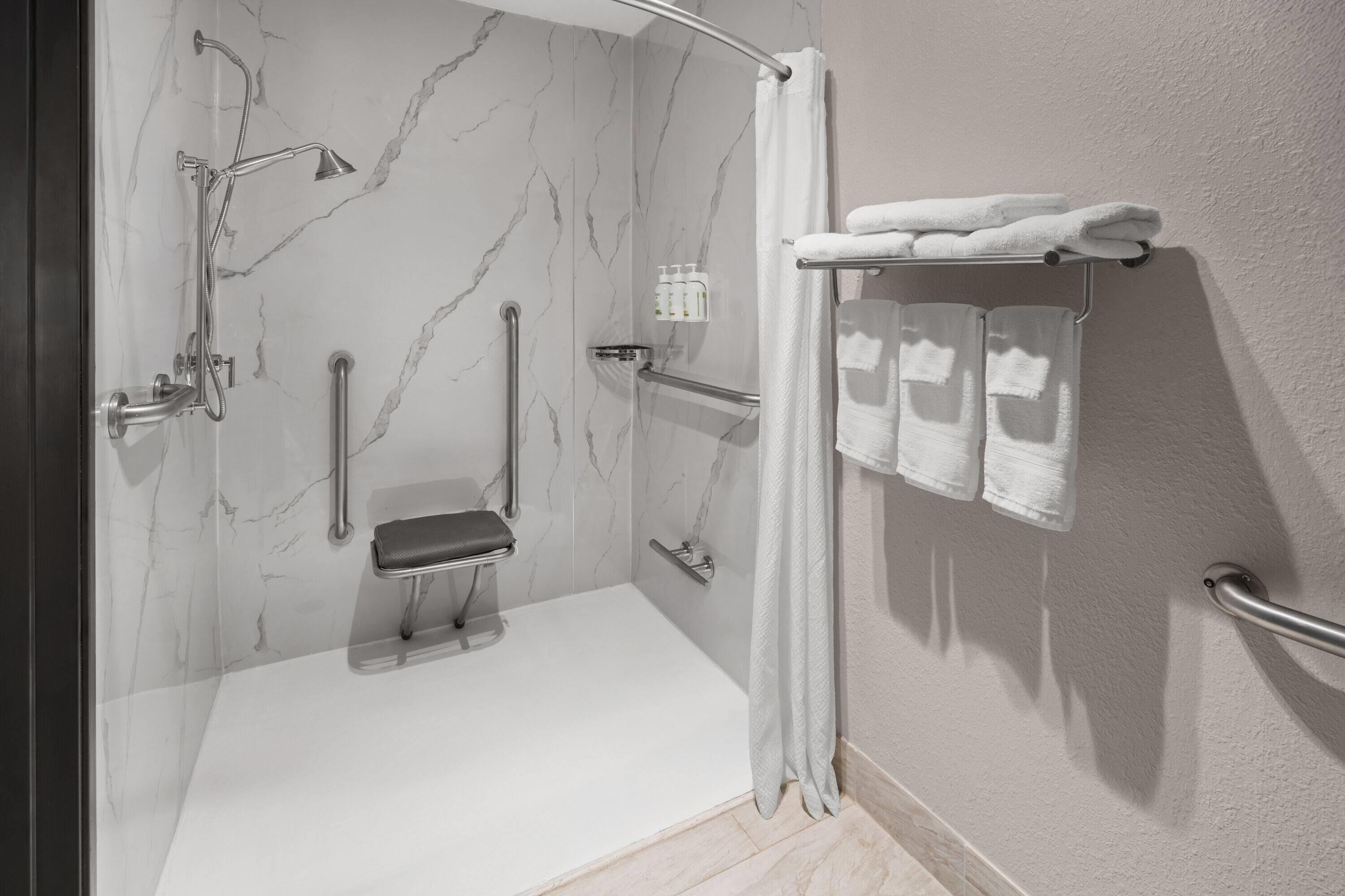 A bathroom with a shower, grab bars, a bench, and a towel rack.