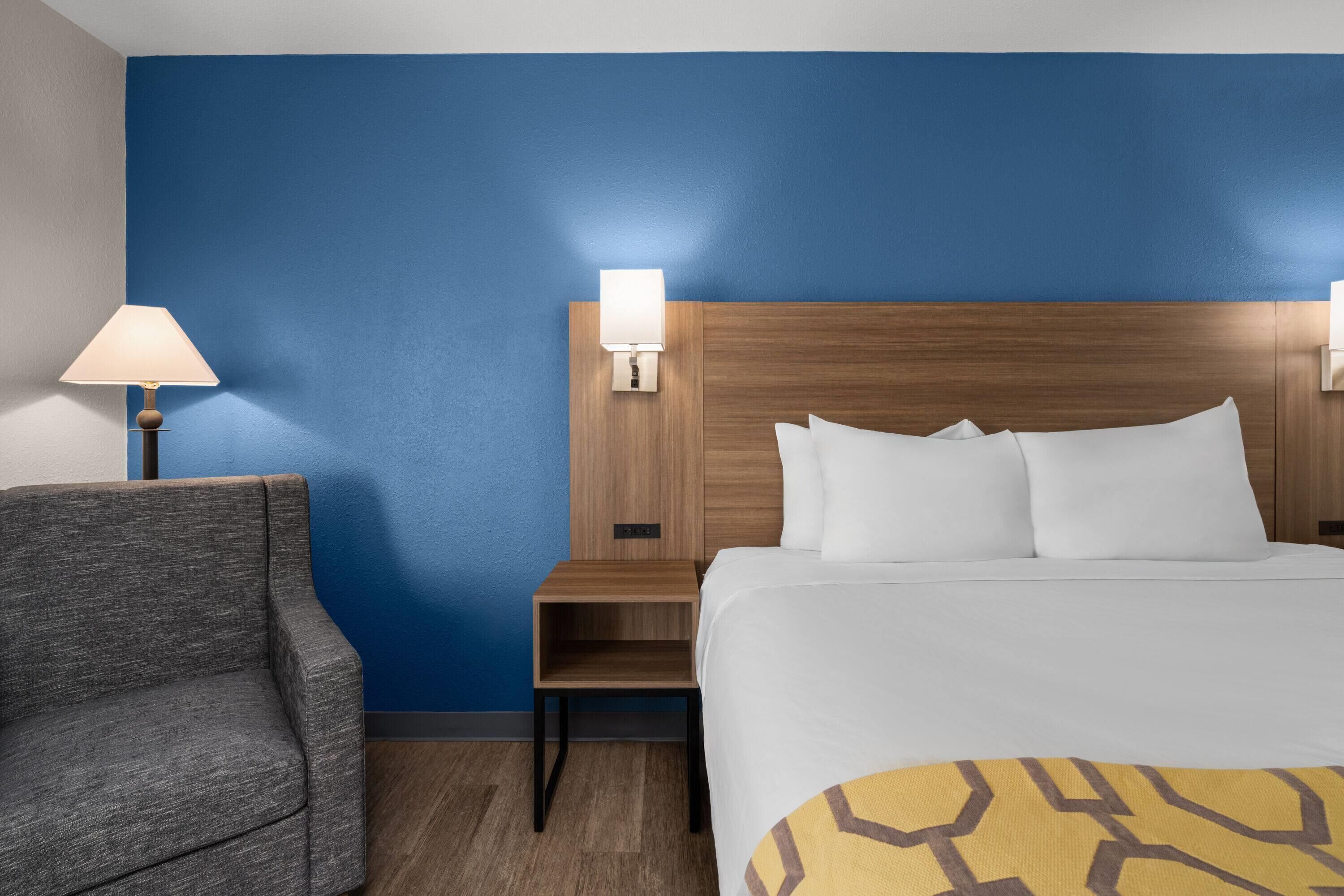 Una habitación de hotel con una cama, una mesita de noche, una lámpara y una silla.
