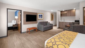 A hotel room with a bed, a sofa, a TV, a small table, a kitchenette, and a bathroom.