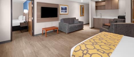 Habitació d'hotel amb llit, sofà, televisió, taula petita, cuineta i bany.