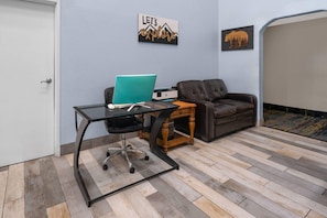 Quarto com uma mesa de vidro, um laptop, uma poltrona de couro marrom, uma mesa lateral de madeira e uma porta.
